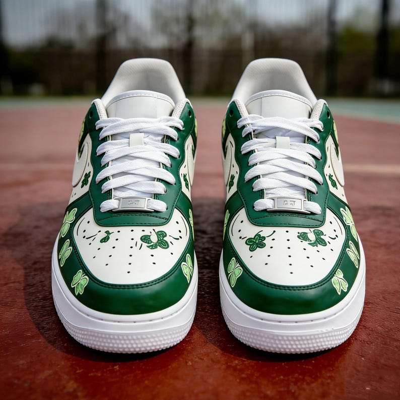 May include: Pair of white and green sneakers with shamrock designs. The shoes have white laces, a white sole, and green accents around the toe, heel, and sides. The shamrocks are in various sizes and are green.