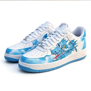 May include: White leather sneakers with blue accents and a dragon design. The shoes feature a blue dragon graphic on the side, cloud patterns, and blue soles. The laces are white, and the shoes have a classic athletic style.