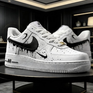 May include: White leather sneakers with black paint drip and splatter design. Features a black Nike swoosh and white laces. The sole is white with the word "AIR" in black.