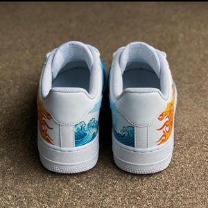 May include: Pair of white sneakers with custom artwork. One shoe features a fiery sun design in orange and yellow, while the other showcases blue ocean waves. The shoes have a white sole and accents.