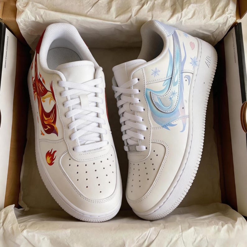 May include: Pair of white sneakers with custom artwork. One shoe features a red and orange phoenix design, while the other showcases a blue and purple icy design with snowflakes. The shoes are in a cardboard box.