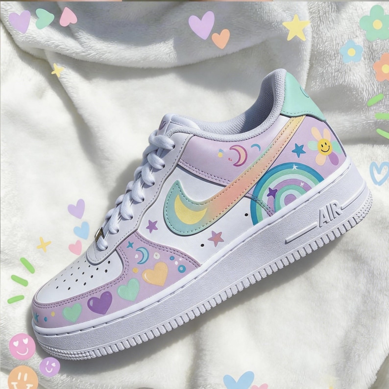May include: White Air Force 1 sneaker with pastel rainbow, moon, star, and heart designs. The Nike swoosh is a pastel rainbow color. The shoe has a white sole and laces. The heel is light green.