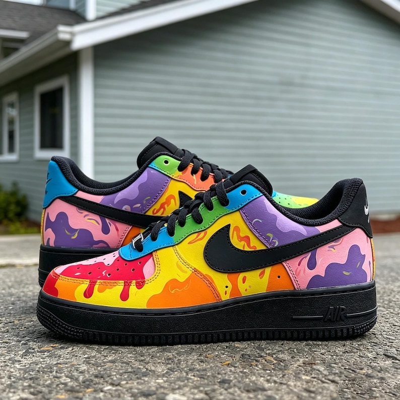 May include: A pair of custom-painted sneakers with a vibrant, colorful design. The shoes feature a black sole and laces, with a rainbow of colors splashed across the upper, including yellow, red, purple, and blue. A black Nike swoosh is visible on the side.
