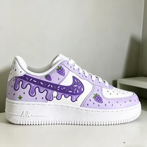 May include: White and purple custom sneakers with a grape-themed design. The shoes feature a white base with purple accents, including a dripping design, grape clusters, and a purple Nike swoosh with sprinkles. The sole is white.