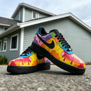 May include: A pair of colorful Nike Air Force 1 sneakers. The shoes feature a vibrant design with a black sole, laces, and swoosh. The upper is decorated with a rainbow-colored drip pattern, creating a bold and eye-catching look.