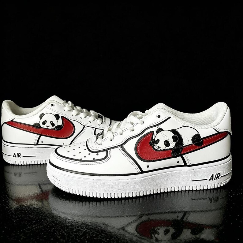 May include: White sneakers with a red swoosh and a panda bear design. The shoes have black accents and the word "AIR" on the side. The panda is lying on the red swoosh.