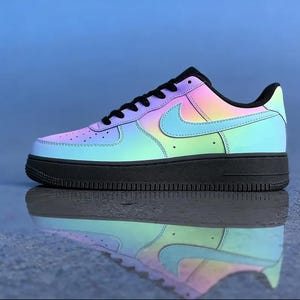 May include: A colorful Air Force 1 sneaker with a gradient design. The shoe features a black sole and laces, with a rainbow-colored upper that transitions from pink to blue and green. The Nike swoosh is light blue.