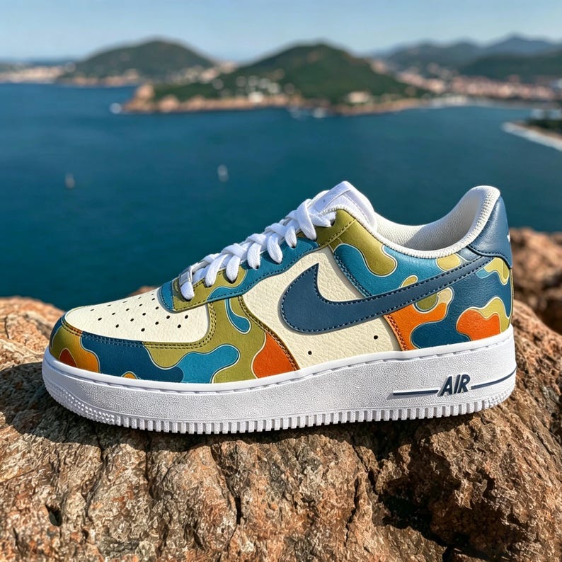 May include: A custom-painted Air Force 1 sneaker with a white sole and a cream-colored upper. The shoe features a blue Nike swoosh and a camouflage pattern in blue, green, and orange. The word "AIR" is printed on the side of the white sole.