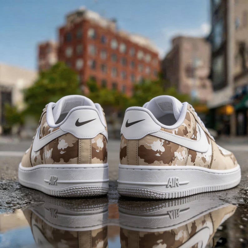 May include: Pair of Nike Air Force 1 sneakers with a camouflage pattern in shades of brown, tan, and white. The shoes have white soles and accents, including the Nike swoosh and the word "AIR". The sneakers are reflected in a puddle.
