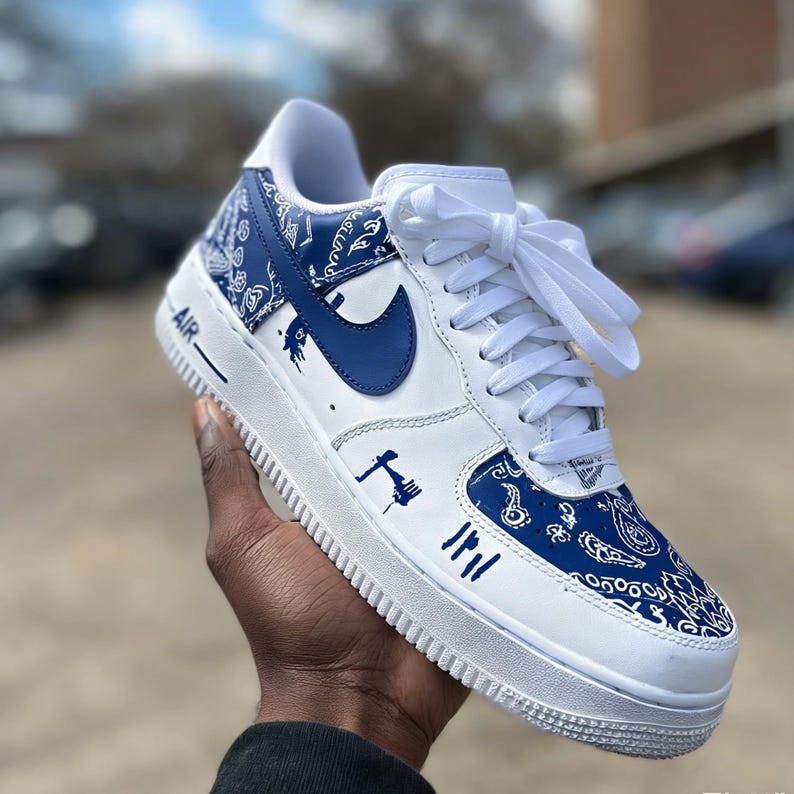 May include: White and blue Air Force 1 sneakers with a paisley pattern on the toe and heel. The Nike swoosh is blue. The shoe has white laces and the word "AIR" is printed on the side.