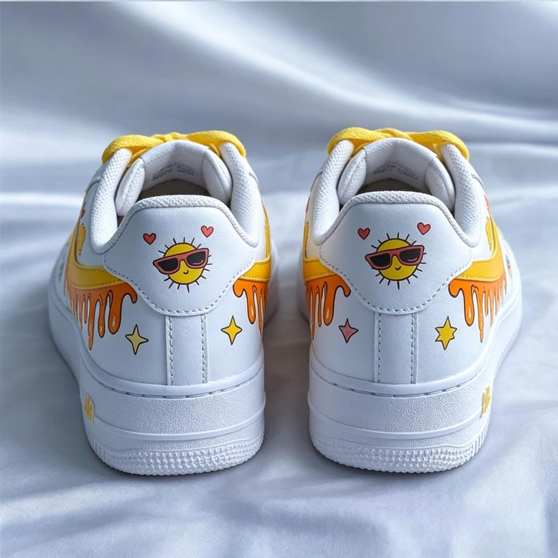 May include: White sneakers with yellow laces and a custom design. The design features a smiling sun wearing sunglasses, hearts, and dripping yellow paint. The shoes have a white sole and a yellow accent on the side.