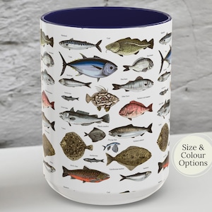 May include: A white ceramic mug with a navy blue interior, covered in illustrations of various fish species. The mug features a variety of colorful fish, including tuna, cod, and flounder. The text "Size & Colour Options" is visible on the side.