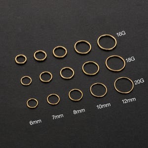Peut inclure: Une collection de boucles d'oreilles créoles dorées de différentes tailles, disposées sur un fond sombre. Les tailles sont indiquées en 6mm, 7mm, 8mm, 10mm et 12mm, avec des jauges 16G, 18G et 20G. Les boucles d'oreilles sont circulaires et semblent être en métal.