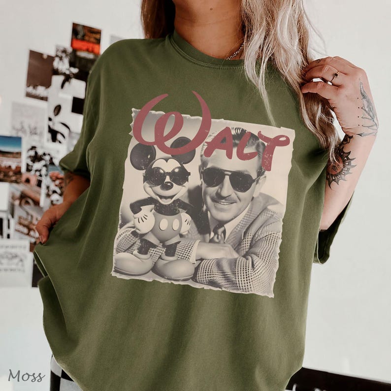 May include: An olive green crewneck t-shirt featuring a graphic print of Mickey Mouse and Walt Disney both wearing sunglasses. The word "WALT" is printed in a large, distressed red font above the black and white photographic image.