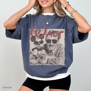 May include: A dark blue oversized t-shirt featuring a graphic print of Walt Disney and Mickey Mouse both wearing sunglasses. The text "Walt" is printed in a large, stylized red font above the black and white image of the two characters.