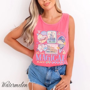 Pu&ograve; includere: Canotta rosa con un design grafico con varie illustrazioni e la scritta "The most MAGICAL PLACE ON EARTH". Il design include immagini di un castello, un treno e altri elementi del parco a tema. La parola "Watermelon" &egrave; stampata in basso a sinistra.