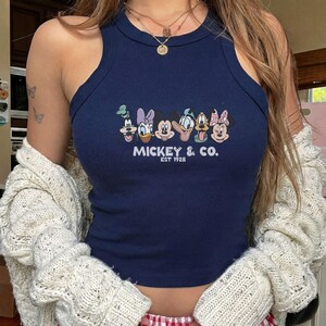 Może przedstawiać: Granatowy top bez rękaw&oacute;w z grafiką Myszki Miki i przyjaci&oacute;ł. Tekst "Mickey & Co. EST 1928" jest wydrukowany pod postaciami. Top ma okrągły dekolt i kr&oacute;j bez rękaw&oacute;w.