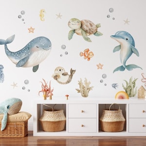 Könnte beinhalten: Aquarell-Wandtattoos mit verschiedenen Meeresbewohnern, darunter ein Wal, eine Schildkröte, ein Delfin und ein Oktopus. Das Design umfasst Blasen, Seesterne und Korallen und schafft ein Unterwassermotto.