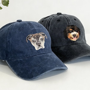 May include: Two baseball caps with embroidered dog faces. One cap is navy blue with a bulldog design, and the other is black with a dog's face. Both caps have a curved brim and a button on top.