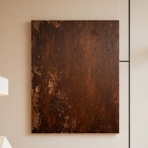 May include: A modern living room featuring a large, rectangular abstract artwork with a distressed, brown finish. The room includes a beige sofa, a black coffee table, and a geometric lamp. The space is illuminated by natural light.