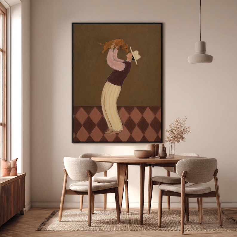 May include: A framed wall art print featuring a stylized illustration of a figure wearing a hat, a pink long-sleeved top, a dark vest, and cream-colored trousers, holding a small brown dog overhead against a dark brown background with a diamond-patterned floor.