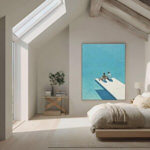 May include: A large framed painting depicts two figures on a white dock over turquoise water. The artwork hangs in a bright, modern bedroom with a bed, side table, and a skylight.