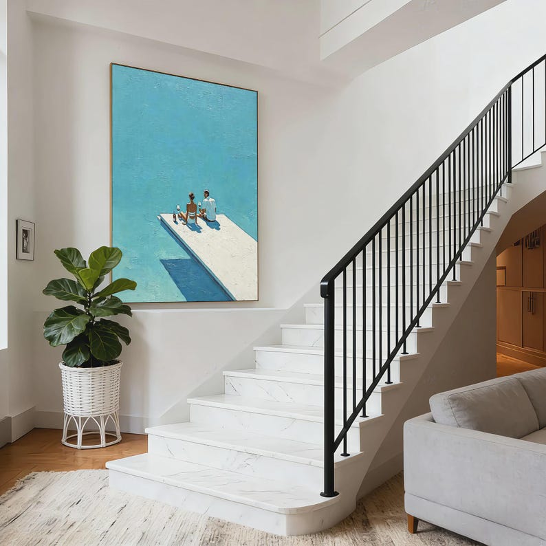 May include: An oil painting depicts two figures on a white diving board over a blue pool. The artwork hangs on a white wall above a staircase with black railings. A large potted plant sits near the stairs.