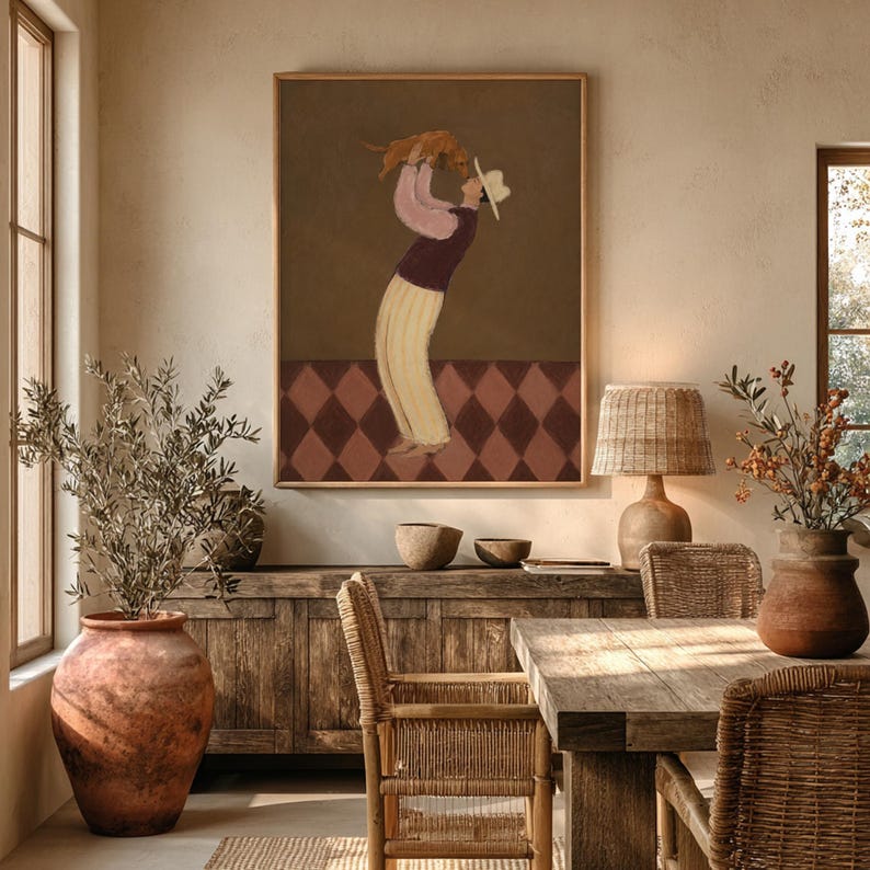 May include: A framed wall art print featuring a person wearing a white hat, a dark purple vest over a light pink long-sleeved shirt, and cream-colored trousers, holding a small brown dog overhead against a dark brown background with a diamond pattern.