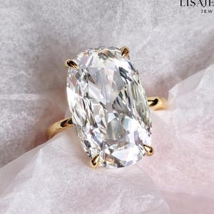 May include: A gold ring with a large, clear, oval-cut gemstone. The ring is set on a white surface, with the text "LISAJEWELRYUK JEWELRY STORE" in the upper right corner.