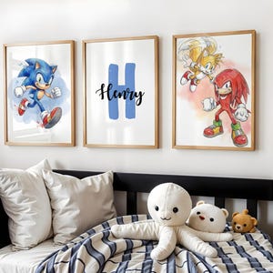 Puede incluir: Tres impresiones enmarcadas con personajes de dibujos animados. Una muestra a Sonic el Erizo corriendo, otra tiene una "H" azul con "Henry" escrito debajo, y la tercera representa a Tails y Knuckles. Las impresiones están en marcos de madera.