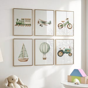 May include: Six framed watercolor prints featuring transportation themes. The prints include a green train, airplane, bicycle, sailboat, hot air balloon, and tractor. Each print has a gold frame and is displayed on a white wall.