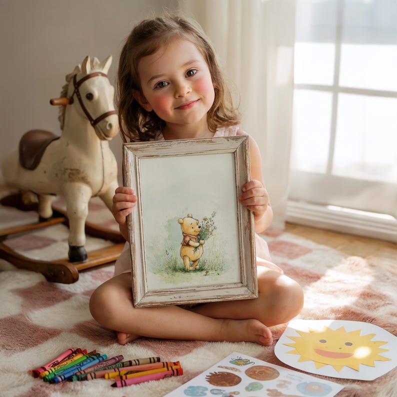 May include: A young girl sits on a pink and white rug, holding a framed picture of Winnie the Pooh. The picture has a distressed white frame. A wooden rocking horse and crayons are also visible.