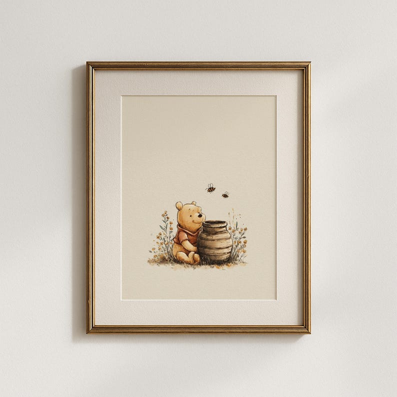 May include: Framed watercolor print featuring a seated yellow bear in a red shirt, next to a brown honey pot. Two bees fly above the pot. The artwork is set against a cream background, framed in a gold-colored frame.