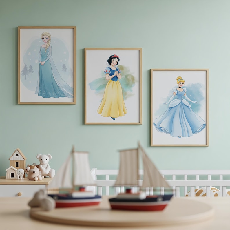 Puede incluir: Tres impresiones art&iacute;sticas enmarcadas con princesas de Disney: Elsa con un vestido azul, Blancanieves con un vestido amarillo y Cenicienta con un vestido de gala azul. Las impresiones est&aacute;n en una pared verde claro, con veleros de juguete y una casa de juguete de madera en primer plano.
