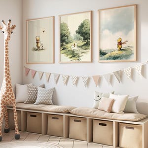May include: Three framed Winnie the Pooh art prints in a child's room. The prints depict scenes of Pooh and friends in a soft, watercolor style. A giraffe toy and a storage bench with pillows and a bunting complete the decor.