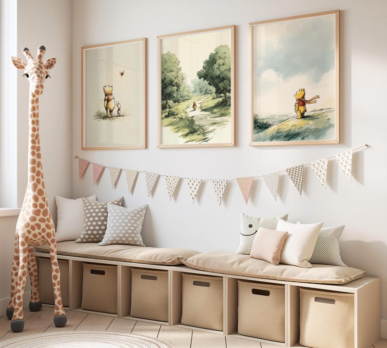May include: Three framed Winnie the Pooh art prints in a child's room. The prints depict scenes of Pooh and friends in a soft, watercolor style. A giraffe toy and a storage bench with pillows and a bunting complete the decor.