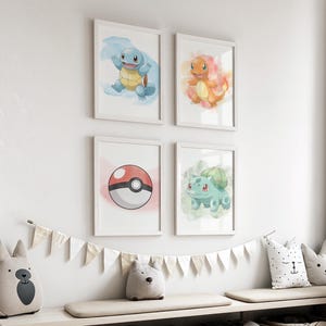 May include: Four framed watercolor prints featuring Pok&eacute;mon characters: Squirtle, Charmander, Bulbasaur, and a Pok&eacute; Ball. The prints are in white frames and are displayed on a white wall. A decorative banner and stuffed animal pillows are below the prints.