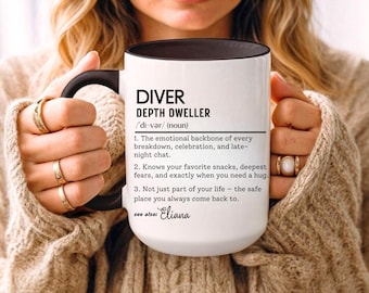 Puede incluir: Taza de cerámica blanca con interior y asa negros, con el texto "DIVER DEPTH DWELLER" y una definición. La taza incluye una definición con tres puntos. La taza es sostenida por una persona que lleva anillos.