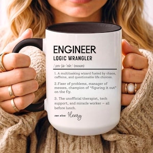 Könnte beinhalten: Weißer Keramikbecher mit schwarzem Innenraum und Henkel. Der Becher zeigt den Text "ENGINEER LOGIC WRANGLER" mit einer Definition. Die Definition enthält Sätze wie "Multitasking-Zauberer" und "inoffizieller Therapeut".