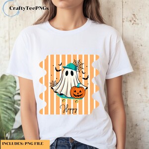Peut inclure: T-shirt blanc avec un motif d'Halloween. Le dessin représente un fantôme de dessin animé portant une casquette turquoise, une citrouille, des chauves-souris et des toiles d'araignées. Le mot "Happy" est écrit en cursive en dessous.