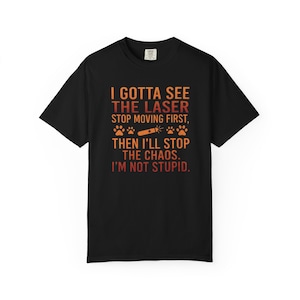 Puede incluir: Camiseta negra con el texto "I Gotta See The Laser Stop Moving First, Then I'll Stop The Chaos. I'm Not Stupid." El texto es en naranja y rojo. La camiseta tiene cuello redondo y mangas cortas.
