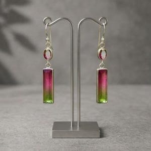 Könnte beinhalten: Ein Paar Ohrhänger mit Silberhaken, jeweils mit einem kleinen ovalen Stein und einem größeren rechteckigen Stein. Die Steine zeigen einen Farbverlauf von Pink nach Grün und sind in polierte Silberfassungen aus Metall eingefasst.