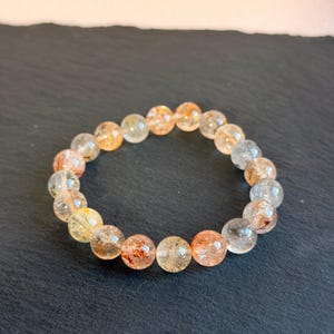 Könnte beinhalten: Ein Armband mit durchscheinenden, runden Perlen in Gelb-, Orange- und Klartönen. Die Perlen sind natürliche Edelsteine. Das Armband wird auf einer dunklen Oberfläche präsentiert.