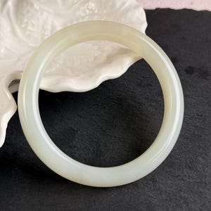 Op de afbeelding: Een gladde, cirkelvormige armband gemaakt van een massieve, doorschijnende gebroken witte steen. De armband heeft een gepolijst, afgerond oppervlak met een consistente dikte over de gehele omtrek, wat een bleek, melkachtig uiterlijk vertoont.