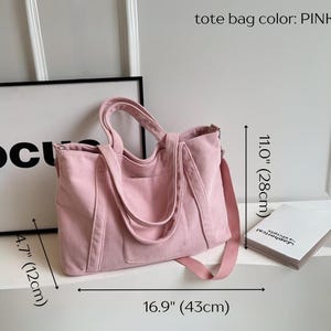 May include: Pink corduroy tote bag with a shoulder strap and handles. The bag is 16.9 inches (43cm) wide, 11.0 inches (28cm) tall, and 4.7 inches (12cm) deep. The text "tote bag color: PINK" is visible.
