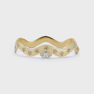 May include: A gold-colored ring with a wavy design. The ring is adorned with small, sparkling gemstones and a larger, marquise-cut stone at the center. The ring has a delicate, elegant appearance.