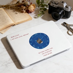 Könnte beinhalten: Weißer Laptop mit blauem Zifferblatt-Design und Apple-Logo. Der Text lautet "DEAR CLOCK I AM YOUR LOYAL SERVANT" und "BUT NOW I HUMBLY ASK YOU TO RELEASE I MUST BE FREE".