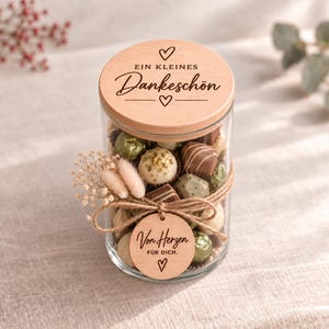 Könnte beinhalten: Ein klares Glasgefäß gefüllt mit gemischten Pralinen, verschlossen mit einem Holzdeckel, der mit dem Text EIN KLEINES Dankeschön und Herzsymbolen graviert ist. Eine Juteschnur hält ein rundes Holzschild mit Von Herzen FÜR DICH und Trockenblumen.