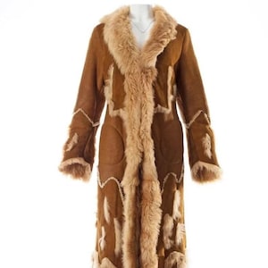 May include: A long, brown coat with a faux fur collar and trim. The coat features a suede-like texture and is adorned with lighter brown fur accents along the front, sleeves, and hem. The coat is displayed on a mannequin.