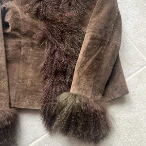 Puede incluir: Chaqueta de ante marr&oacute;n con ribete de piel en los pu&ntilde;os y la parte delantera. La chaqueta tiene mangas largas y un corte entallado. El ribete de piel es de un tono marr&oacute;n m&aacute;s oscuro, a&ntilde;adiendo textura.